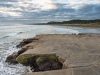 rocks next to the water in the middle of the beach and waves coming ashore on the shore