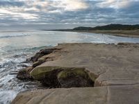 rocks next to the water in the middle of the beach and waves coming ashore on the shore