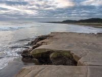 rocks next to the water in the middle of the beach and waves coming ashore on the shore