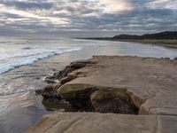 rocks next to the water in the middle of the beach and waves coming ashore on the shore