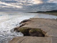 rocks next to the water in the middle of the beach and waves coming ashore on the shore