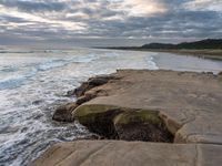 rocks next to the water in the middle of the beach and waves coming ashore on the shore