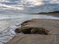 rocks next to the water in the middle of the beach and waves coming ashore on the shore