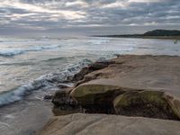 rocks next to the water in the middle of the beach and waves coming ashore on the shore