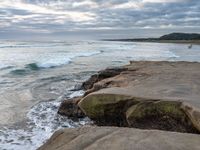 rocks next to the water in the middle of the beach and waves coming ashore on the shore