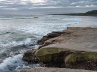 rocks next to the water in the middle of the beach and waves coming ashore on the shore