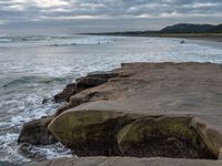 rocks next to the water in the middle of the beach and waves coming ashore on the shore