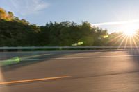 a person riding a motorcycle on the street at sunset with sun glaring through trees behind it