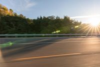 a person riding a motorcycle on the street at sunset with sun glaring through trees behind it