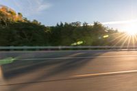 a person riding a motorcycle on the street at sunset with sun glaring through trees behind it