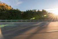 a person riding a motorcycle on the street at sunset with sun glaring through trees behind it