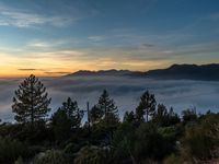 a person is sitting on a bench looking at the sunrise above the fog filled mountains