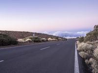 an empty winding road on a mountain with the sun set above the mountains in the background