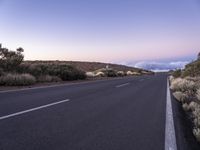 an empty winding road on a mountain with the sun set above the mountains in the background