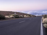 an empty winding road on a mountain with the sun set above the mountains in the background