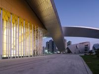 a large modern structure with lots of glass and metal on it at dusk, along with the light on outside