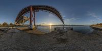 the sun sets behind an arch and sets on the shore of water with rocks by