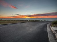 an empty road with sunset over the ocean on the horizon behind it in long beach, ca