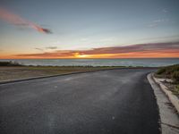 an empty road with sunset over the ocean on the horizon behind it in long beach, ca