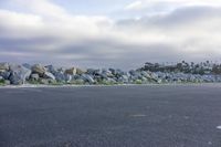 a large group of rocks near the ocean shore with an empty parking lot in front of them