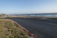 an empty road near a beach and waves as well as cars on the sand and houses on the beach