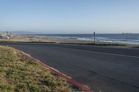 an empty road near a beach and waves as well as cars on the sand and houses on the beach