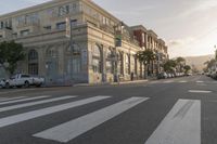 the sun goes down on the town street and there are cars parked on the curb