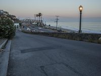 a traffic light on a deserted city street by the ocean at dusk, with cars driving by