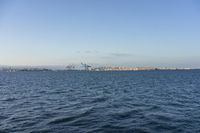 blue water with small waves in the foreground and some cranes at the horizon in the background