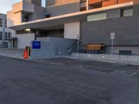 empty parking lot next to grey buildings with street signs and trees at dusk in front