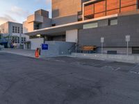 empty parking lot next to grey buildings with street signs and trees at dusk in front