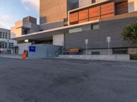 empty parking lot next to grey buildings with street signs and trees at dusk in front