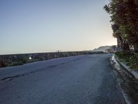 an empty street next to a building on a hillside with trees near by and in the distance