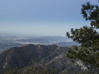 a view of a valley with pine trees from a mountain top looking over a city and hills