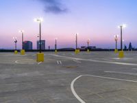 an empty parking lot with street lights next to it at dusk, taken from the road