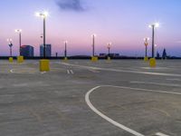 an empty parking lot with street lights next to it at dusk, taken from the road