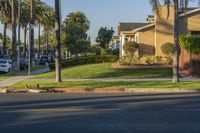 a road in the neighborhood with cars parked near the curb and palm trees on either side