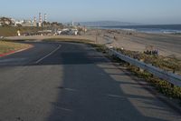 an empty road near a beach and waves as well as cars on the sand and houses on the beach