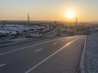 an empty road with cars parked on both sides and a sunset behind it in the distance