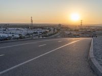 an empty road with cars parked on both sides and a sunset behind it in the distance