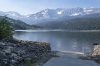 a person on the sidewalk is looking at a large body of water surrounded by mountains