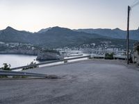 the car is driving through a curve on the road with mountains in the background and a city near the water