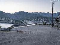 the car is driving through a curve on the road with mountains in the background and a city near the water