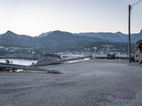 the car is driving through a curve on the road with mountains in the background and a city near the water