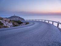 a curved road near a lighthouse, overlooking the ocean at sunset from below it is visible