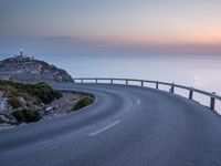 a curved road near a lighthouse, overlooking the ocean at sunset from below it is visible