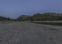 a dirt path leading to a river and rocky slope with a boat on it at dusk