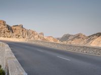 a road with rocks at the edge is next to a mountain with no cars on it