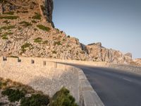 a road with rocks at the edge is next to a mountain with no cars on it