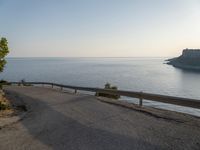 a road in front of a cliff overlooking the water and coastline with a bench next to it